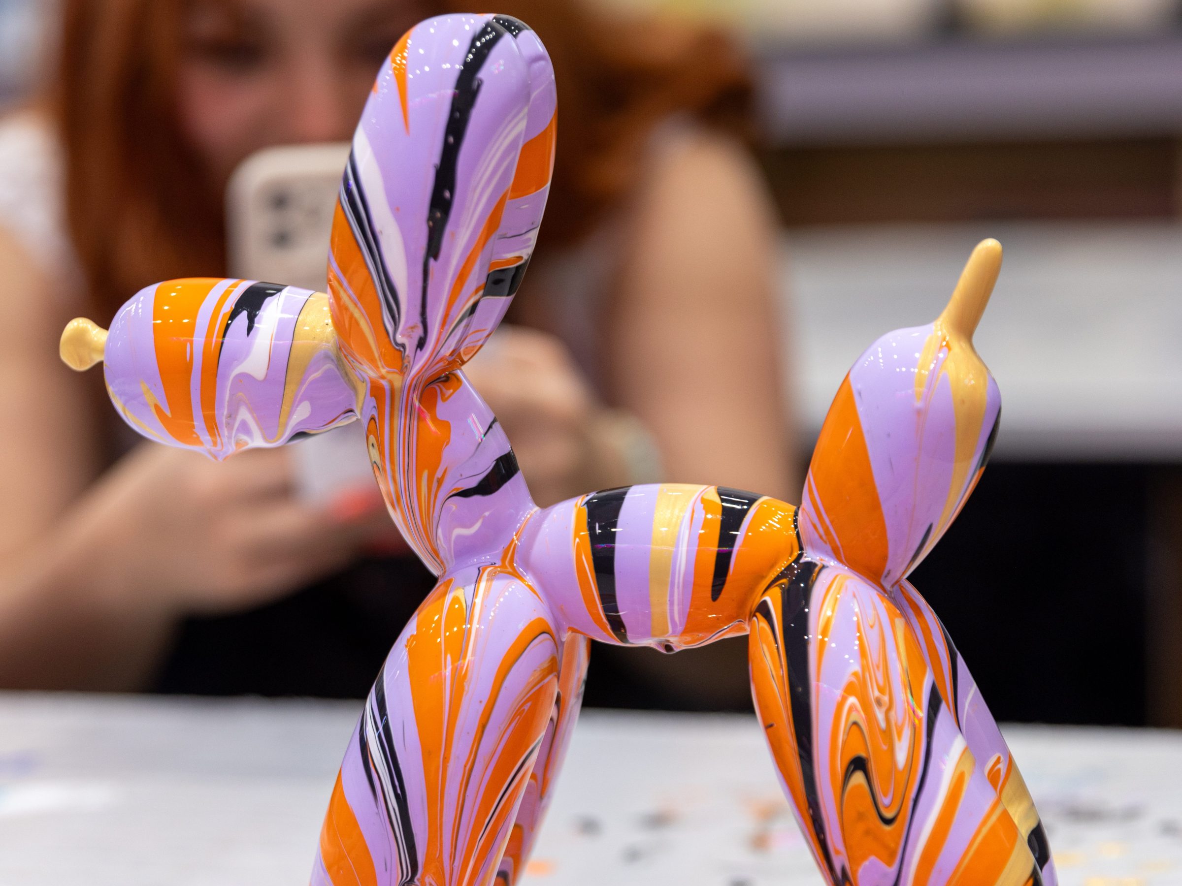 Colorful balloon dog sculpture with marbled pattern, person photographing in background.