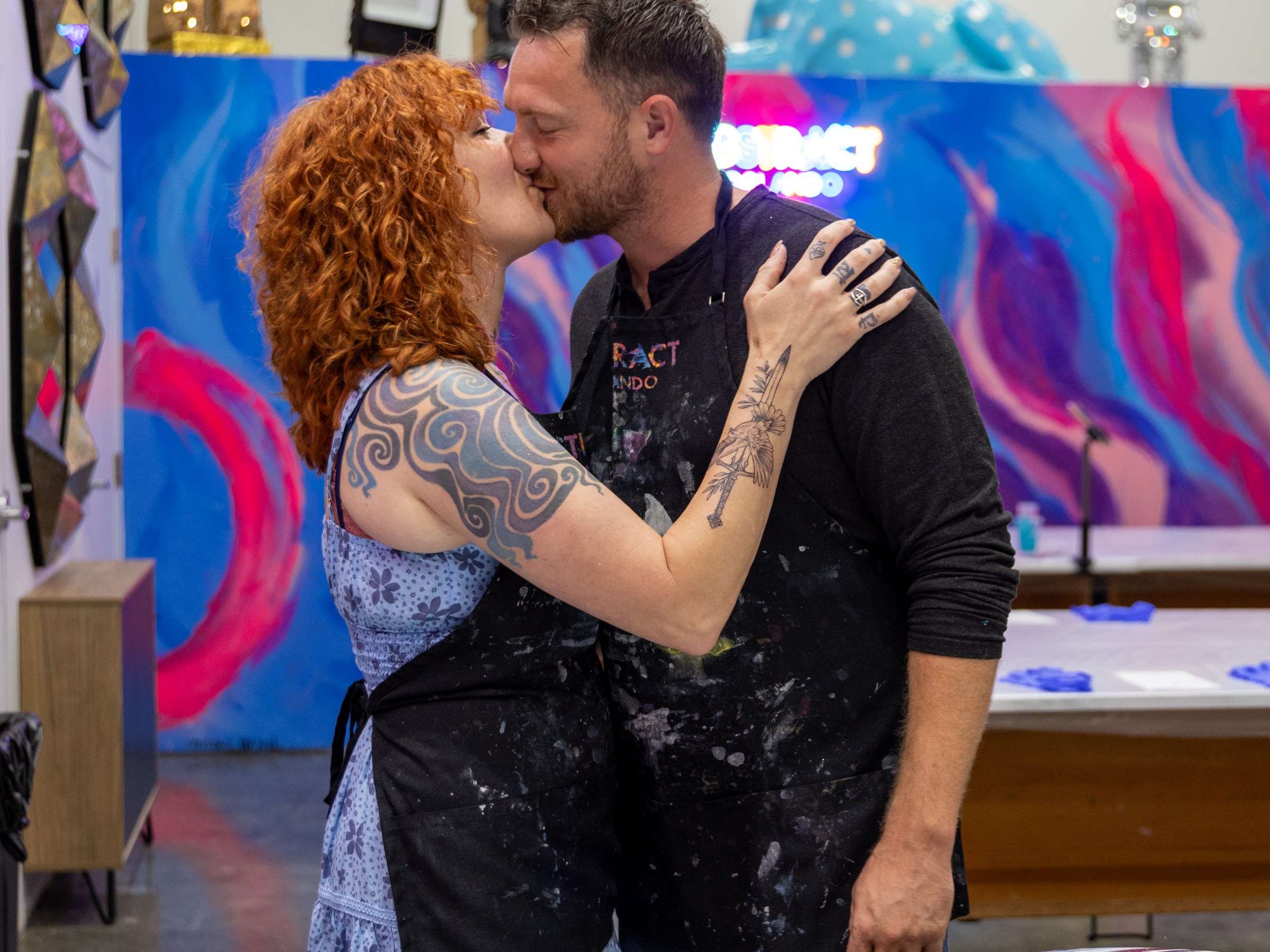 Couple kissing in art studio with colorful background and paintings.