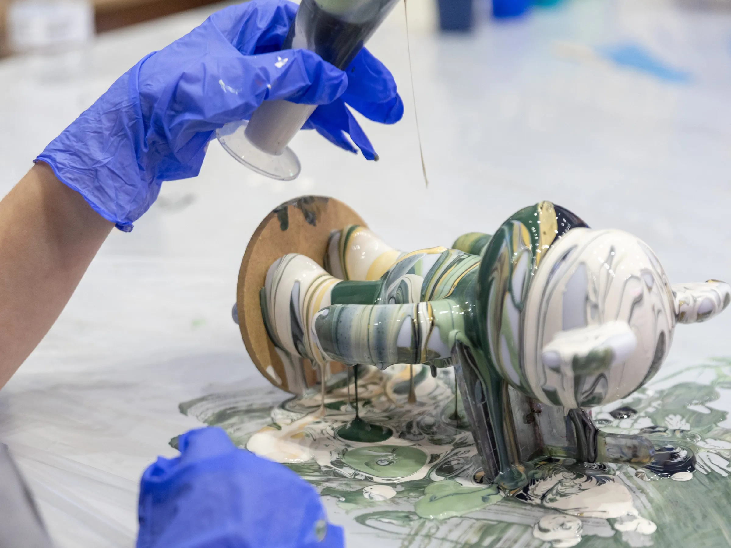 Person with gloves pouring paint over a sculpture on a table.