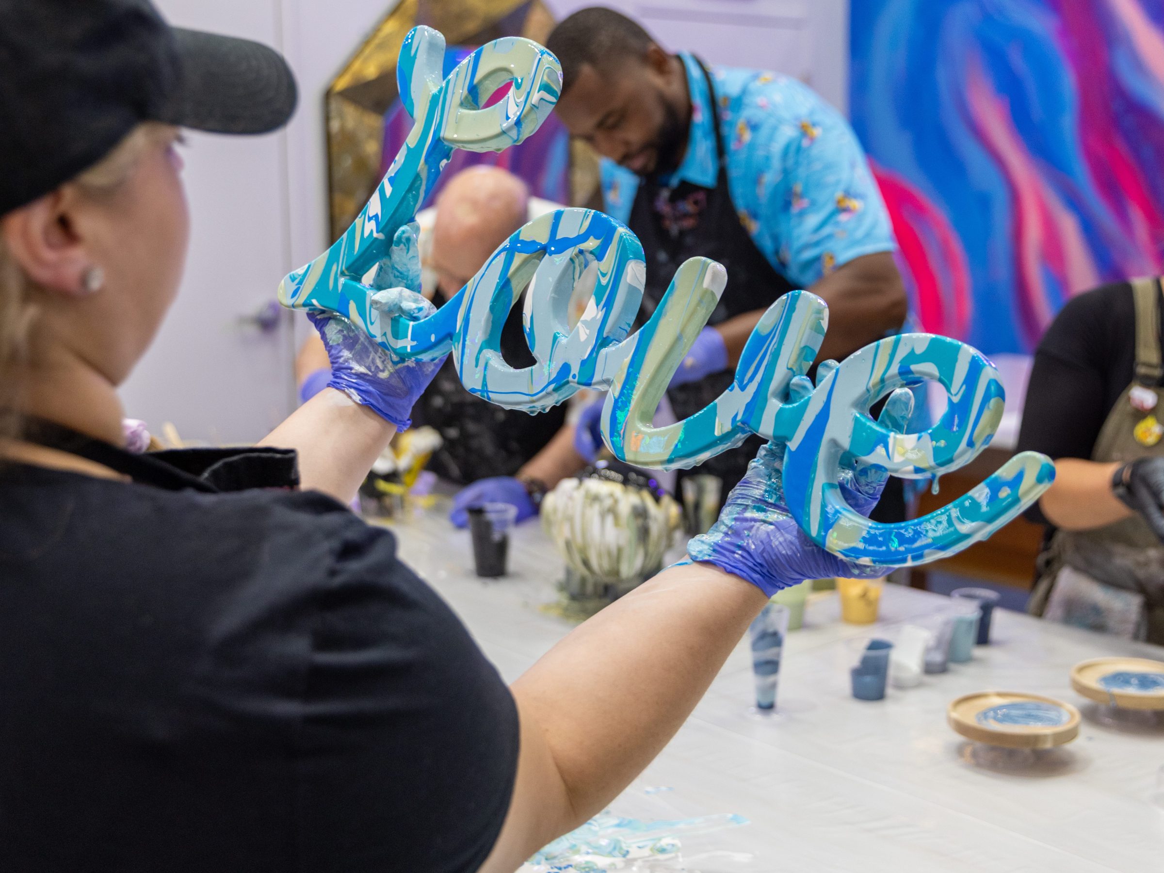 Person holding a decorative 'Love' sign in a colorful art studio.