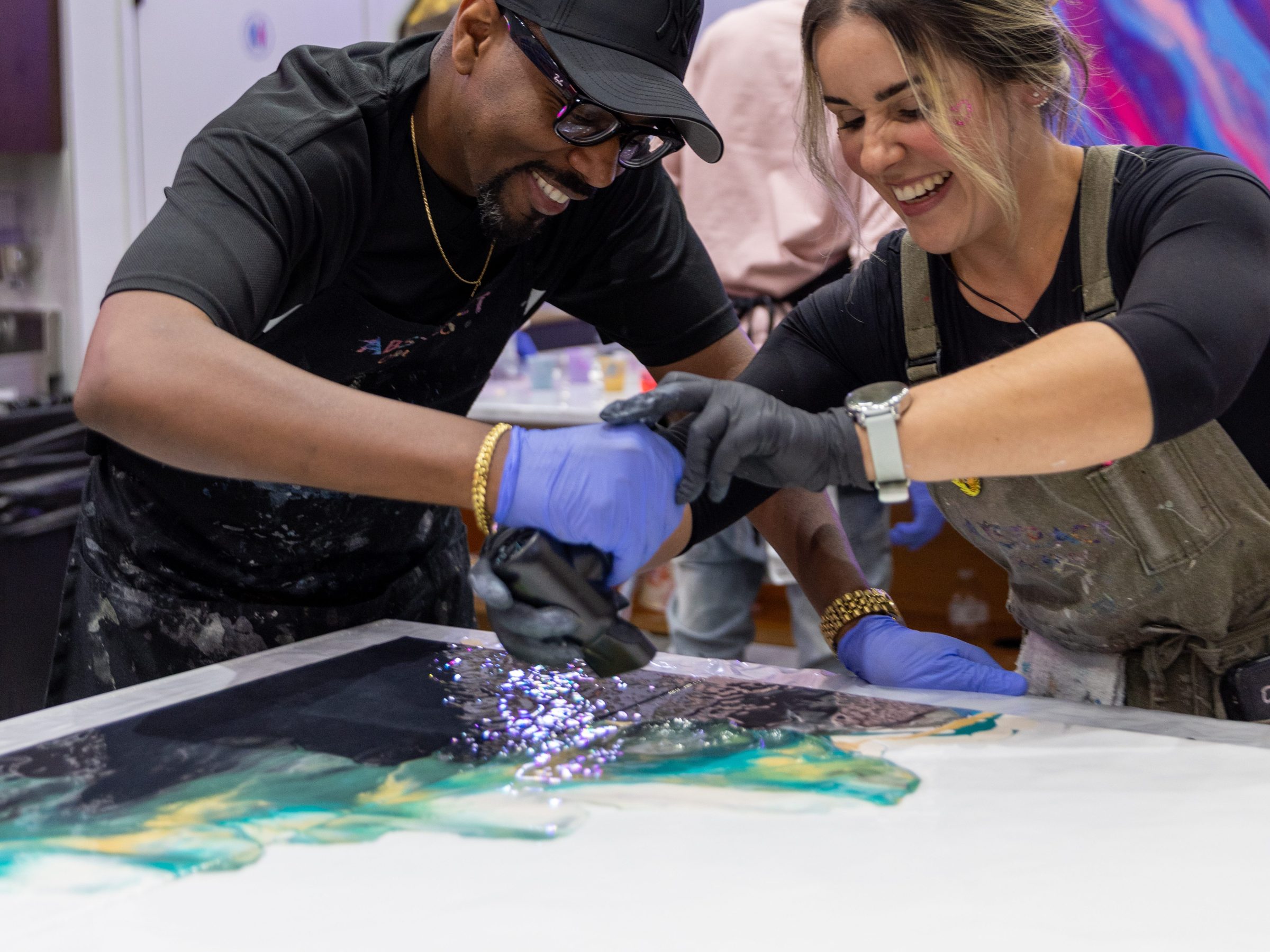 Two artists smiling while creating a colorful painting together.
