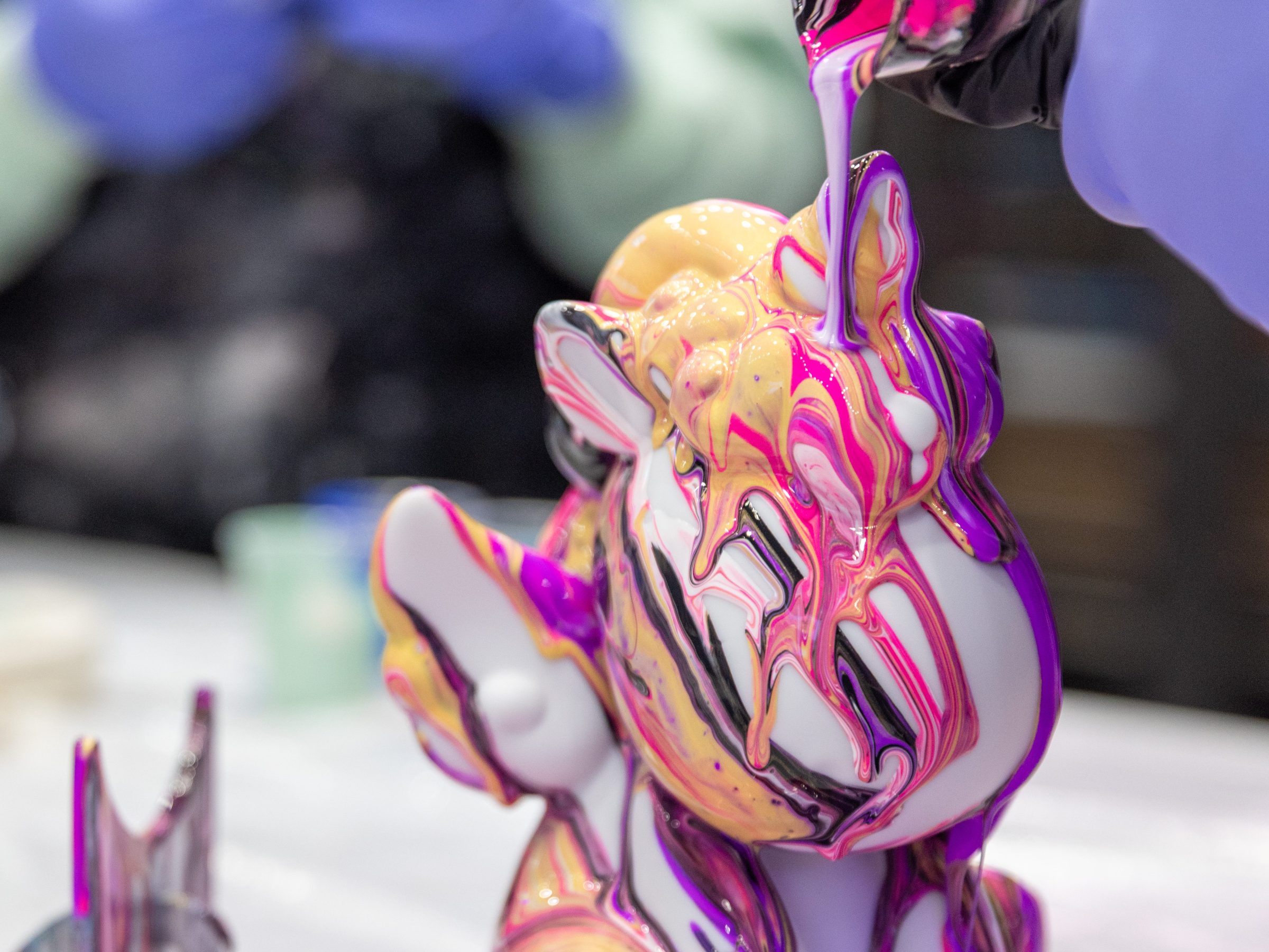 Colorful paint poured over sculpture on table, with purple gloves.