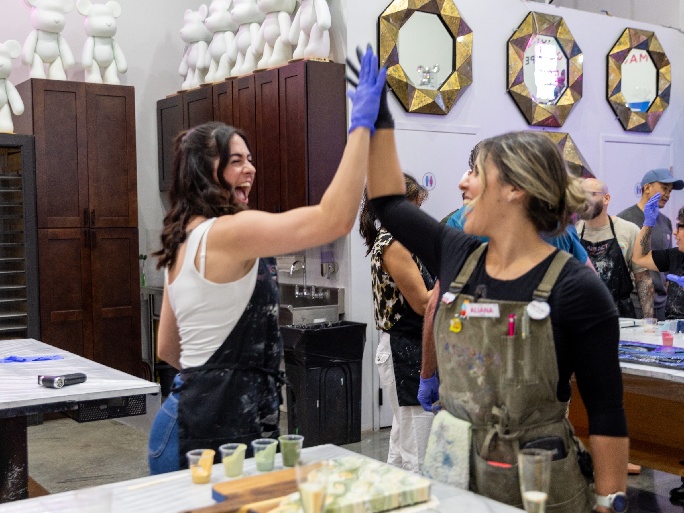 Two women in aprons high-fiving in an art studio.