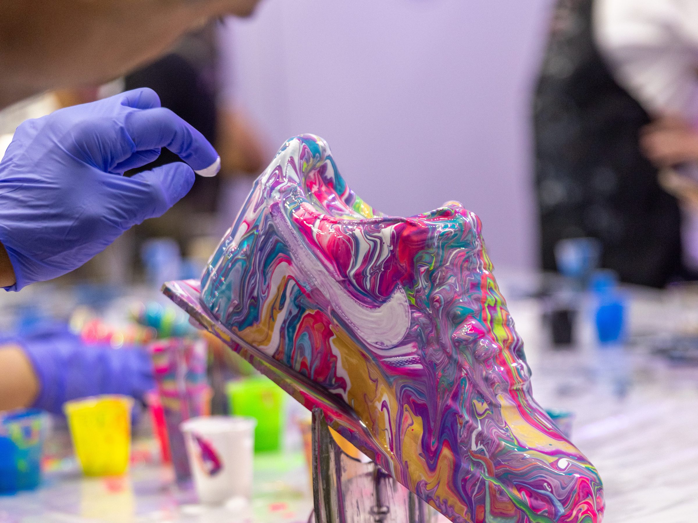 Custom sneaker being painted with colorful, abstract patterns by a person wearing gloves.