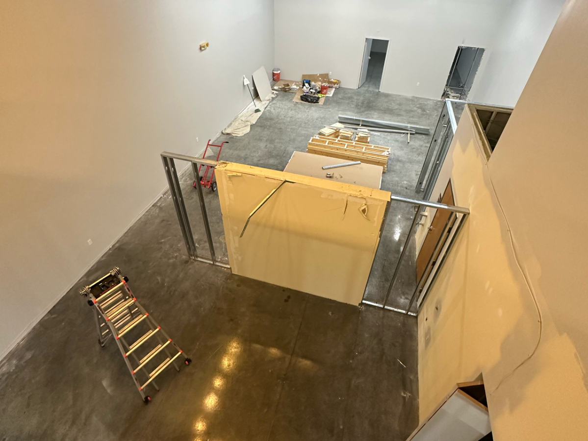 View of a large room under construction with a ladder and building materials.