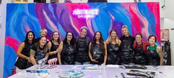 Group of people in aprons posing in front of a colorful abstract mural under a neon sign.
