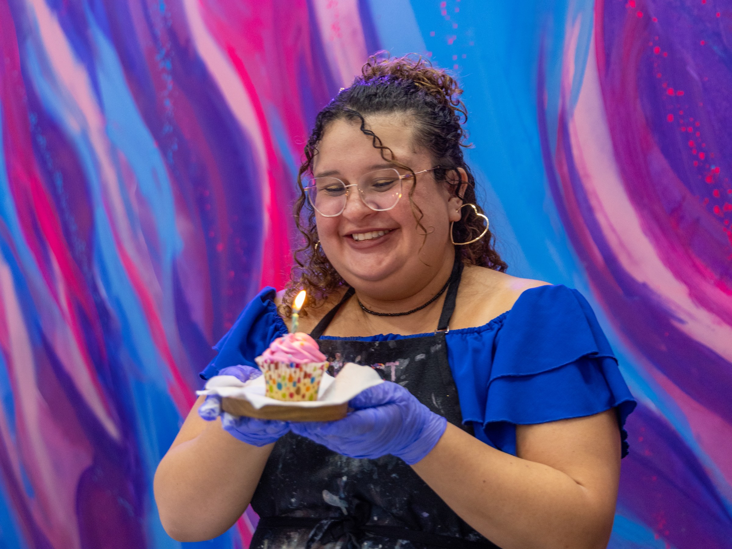 Person holding dessert with a candle, against a colorful abstract background.